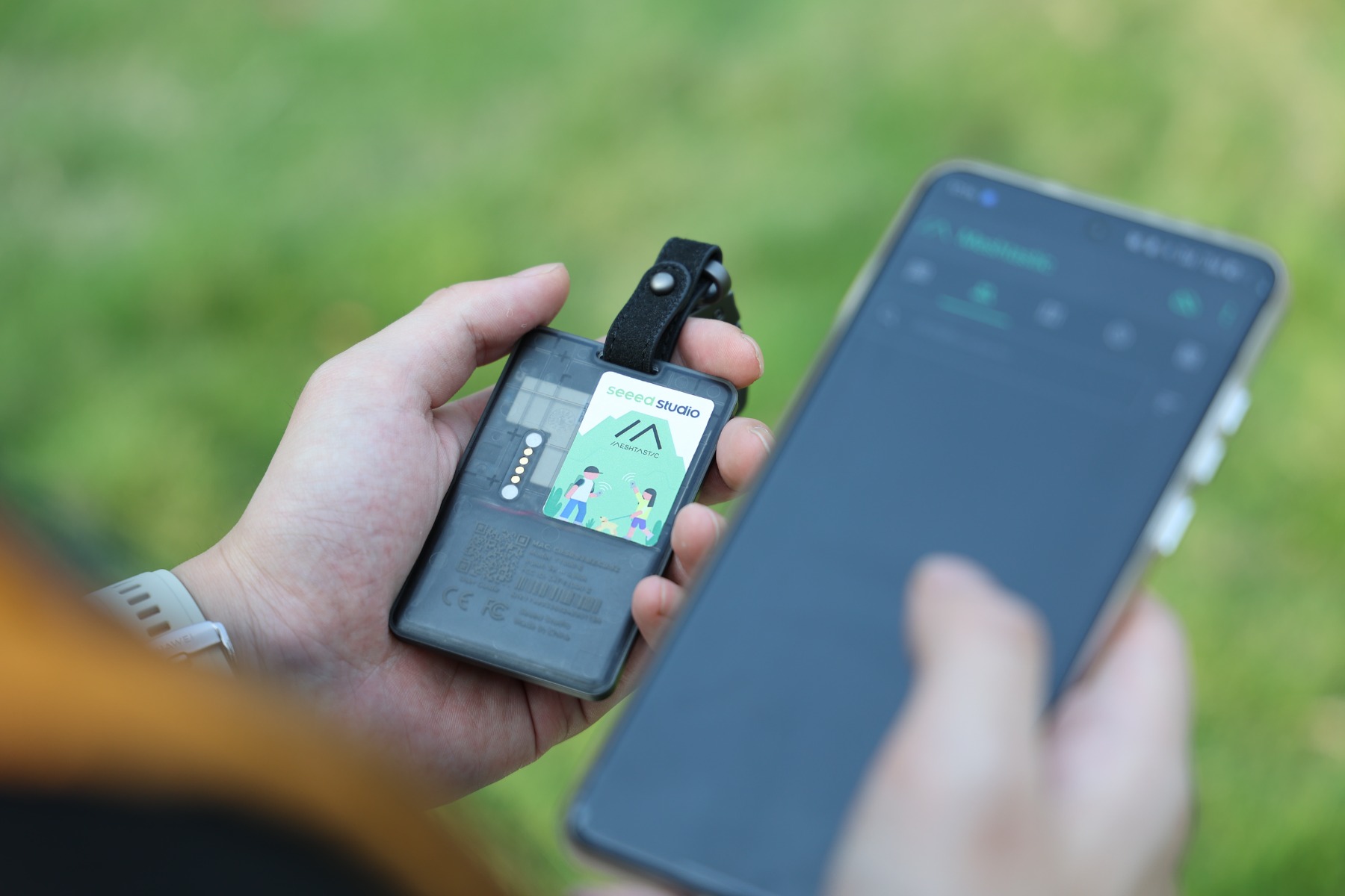Meshtasticアプリを表示したスマートフォンの隣でSenseCAP T1000-Eを手に持っているところ